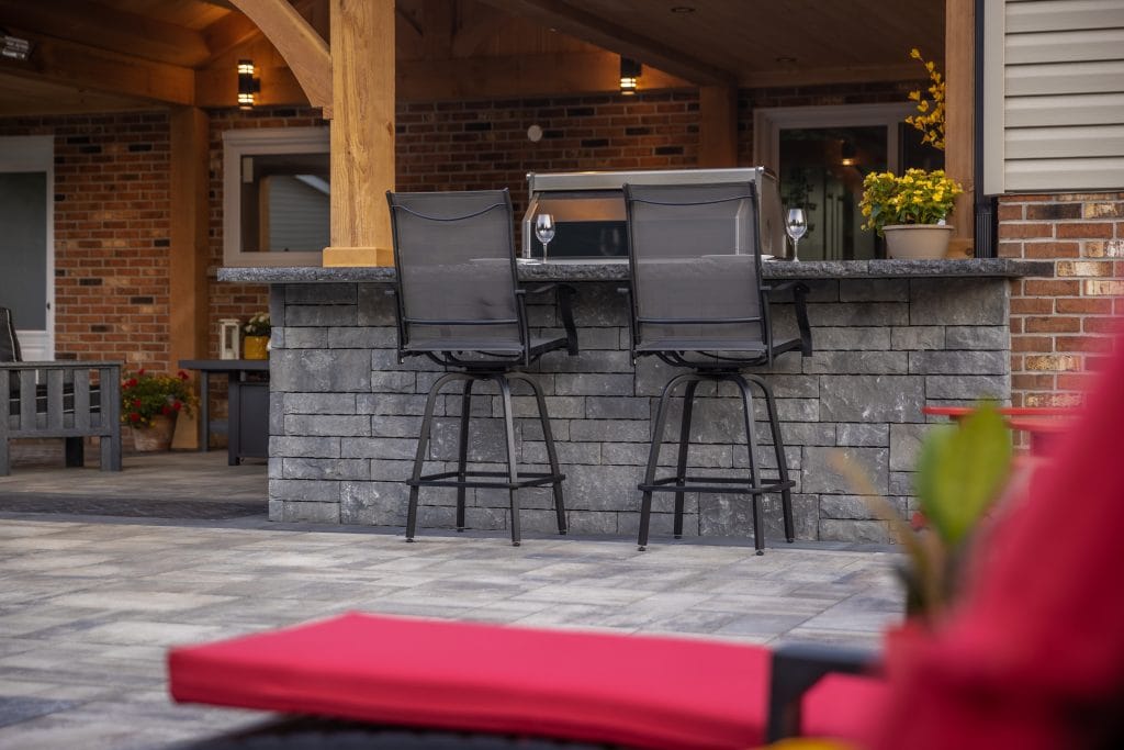 Outdoor bar seating beside a backyard pool and stone patio